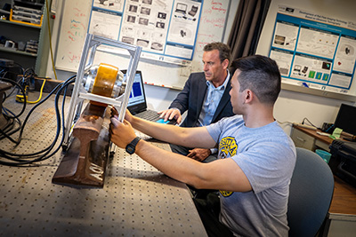 Huang holds a metal frame with a wheel inside over a segment of railroad track