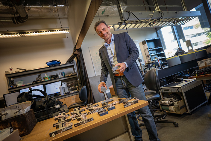 Lanza di Scalea holds a railroad tie, standing beside a table with a variety of railroad ties laid on it.
