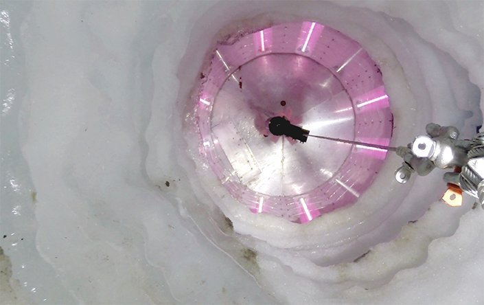 Looking into an icy borehole lit up by pink UV lights