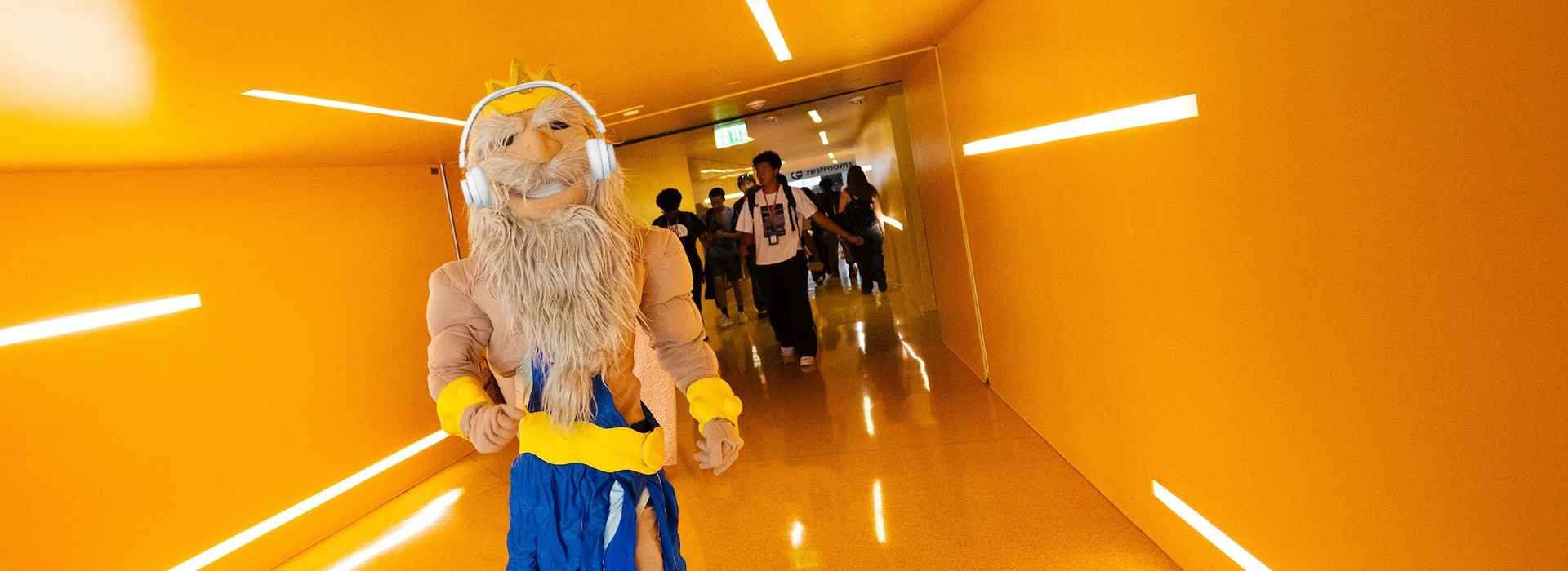 King Triton wearing headphones walking in yellow hallway.
