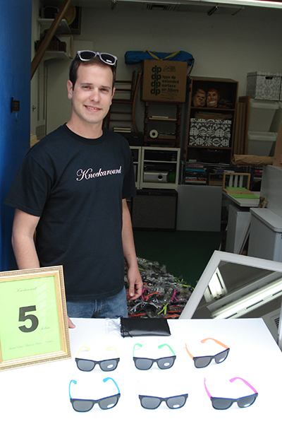 Graduate student Adam Moyer in the doorway of his Visual Arts studio, with six pairs of sunglasses on a table.