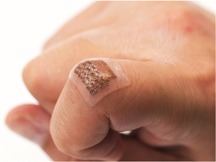 A square-shaped sticker with small electronic circuits on the joint of a person's finger.