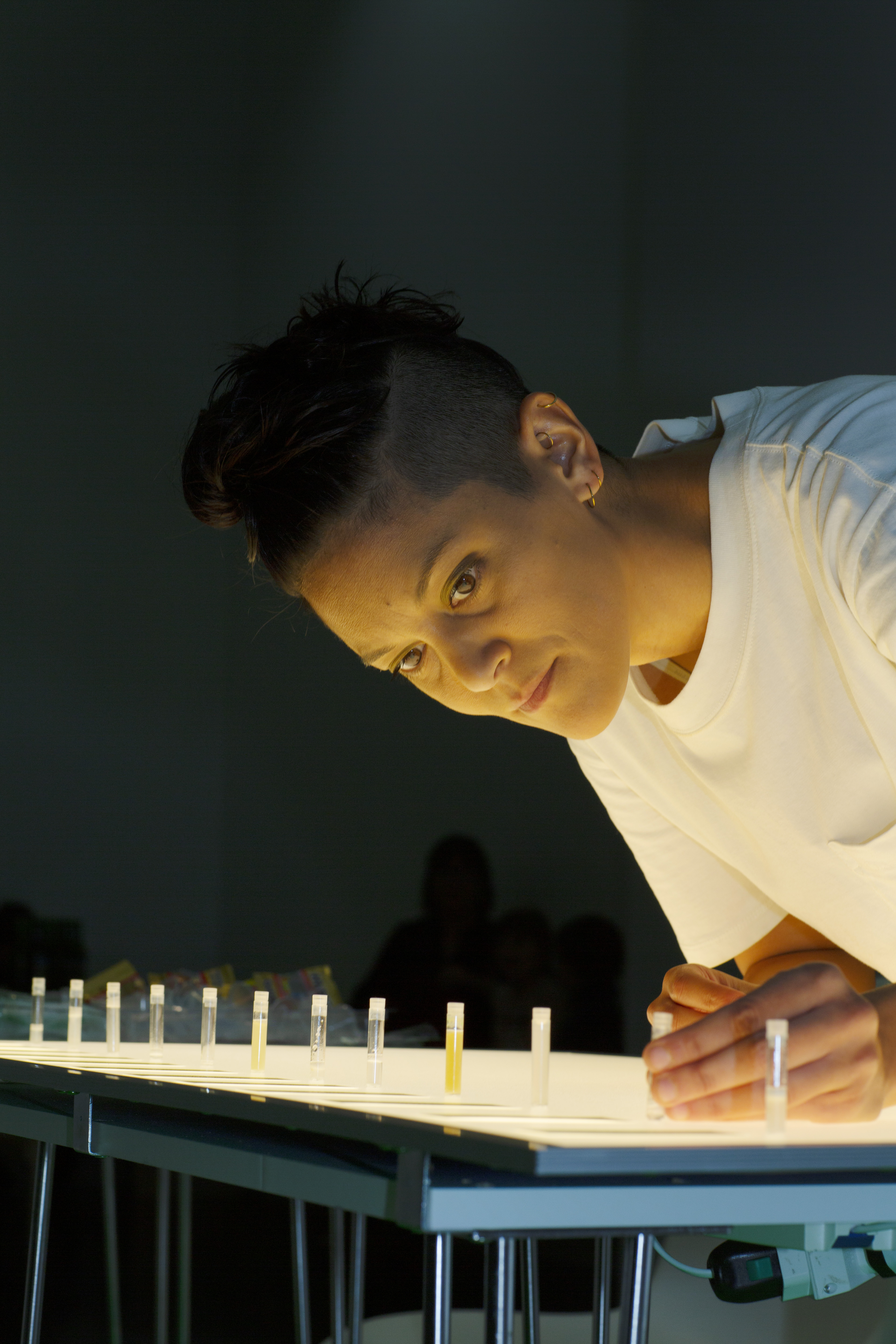 The artist leans over a table with vials of saliva