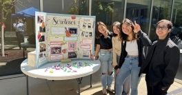Four students standing near a poster that reads 