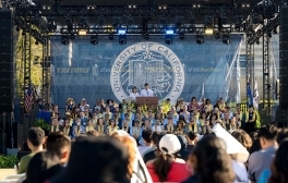 Two students stand behind podium facing new Tritons as faculty members look on