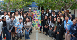 25 people smile and pose with a colorful piece of artwork