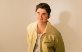 Nicky Youre wears a yellow jacket and stands in a fluorescent pink light.