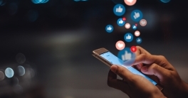 Social media concept image of hands holding a phone with social-media like and heart icons floating off the screen