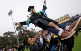 Graduating students smile and wave in cap and gown as they process down the center aisle on commencement day.