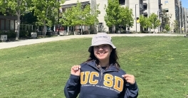 Siono Gutierrez wearing a UC San Diego hat and shirt in front of Jacobs Hall.