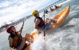 Two UC San Diego women students sitting in a tandem kayak paddling into the waves on La Jolla Shores beach.