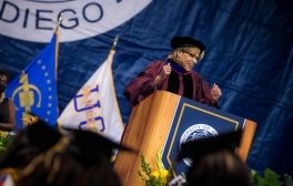 Vice Chancellor for Equity, Diversity, and Inclusion Becky R. Petitt lifts her fists up in triumph at the podium during a commencement celebration.