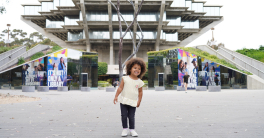 A young child smiling stands outside of Geisel Library at UC San Diego.