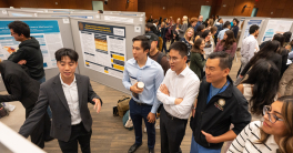 Room overview photo of groups of people looking at research posters. 