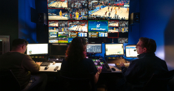 Video: Three people sit at a bank of monitors in a dark room