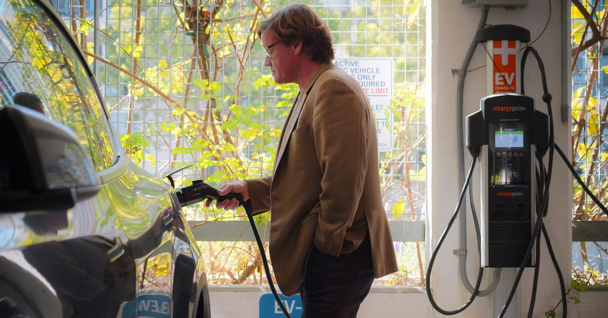 A person plugs in an electric vehicle that is parked in a parking garage.