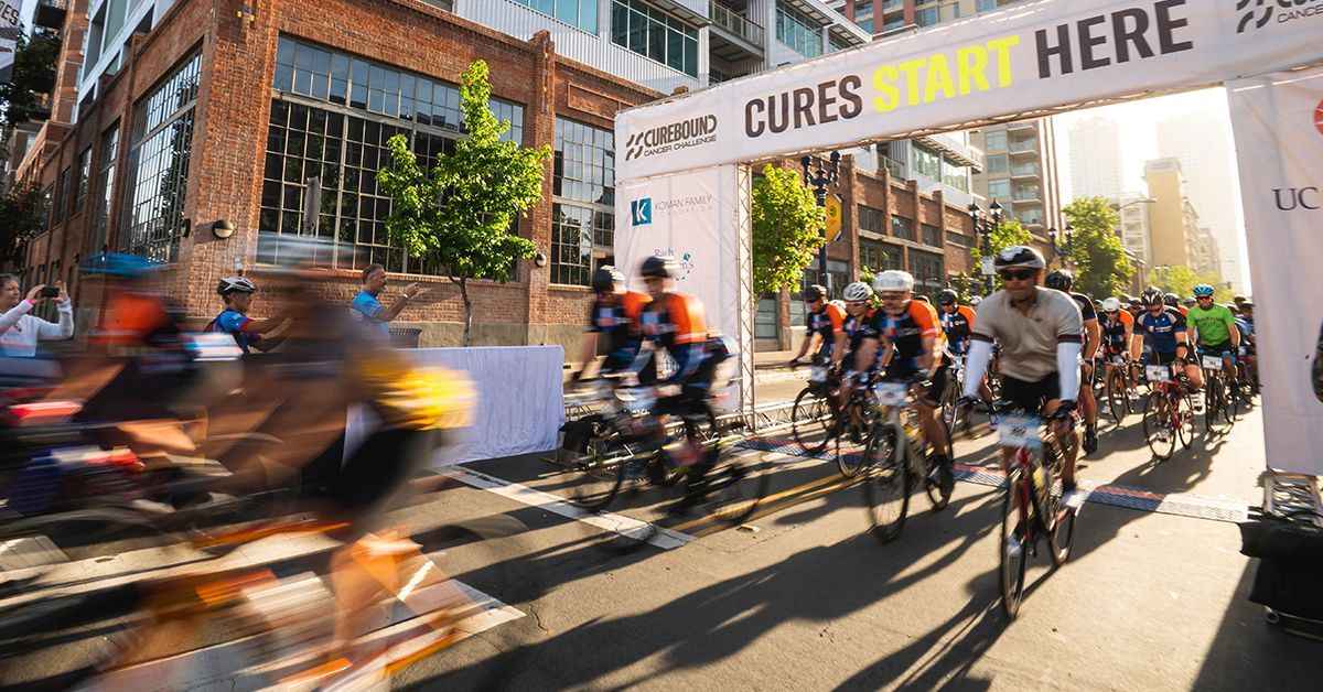 Cyclists cross a finish line with Curebound banner above them. 