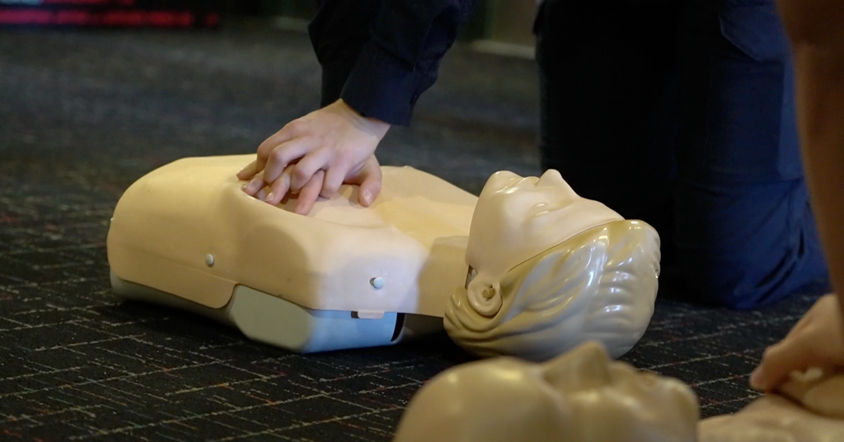 Maureen O'Connor is performing CPR on a mannequin. Her hands are locked together across the mannequin's chest. 