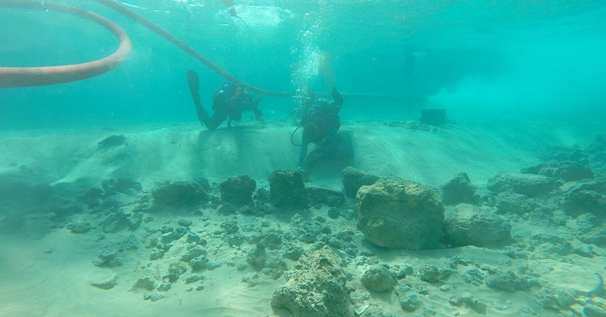 Two divers examine the remains of a stone wall on the seabed.