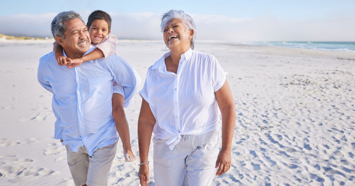 Two adult seniors walking on the beach with a child