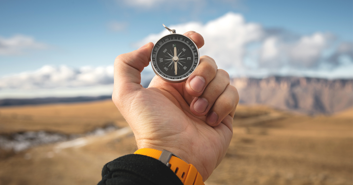 A hand holding a compass on a hiking trail