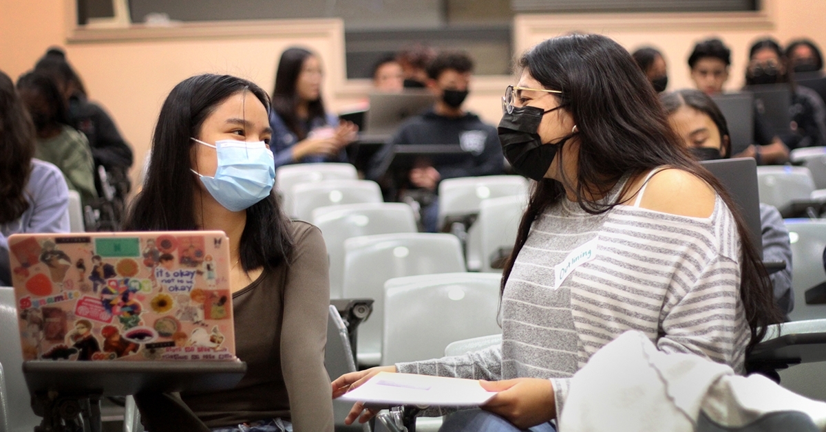 A UC San Diego undergraduate student sits with a local high school student in a lecture hall to give personalized feedback on her personal insight questions as she prepares to submit a University of California application.