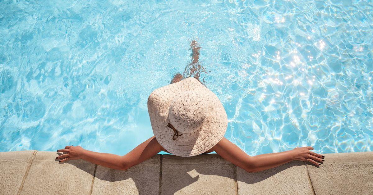 Person wearing sun hat leans back against edge of swimming pool