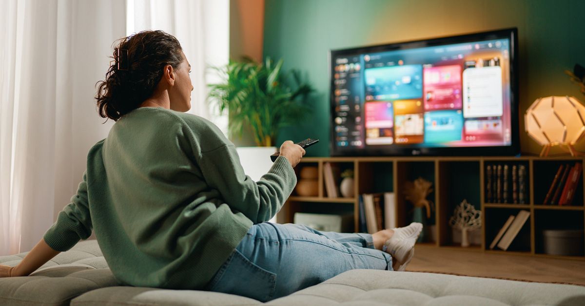 Person on sofa holds remote toward streaming service menu displayed on TV