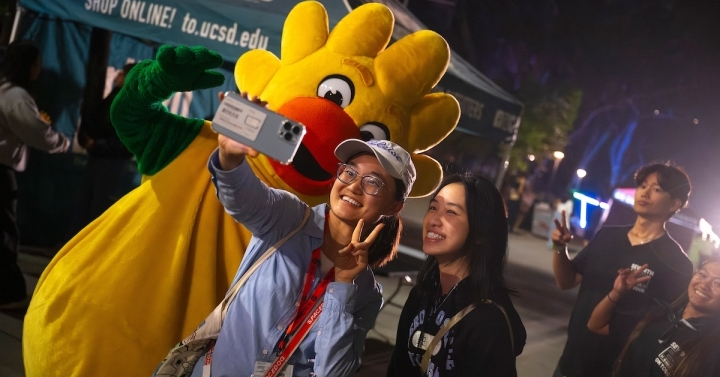 Two students take a selfie next to a sun mascot.