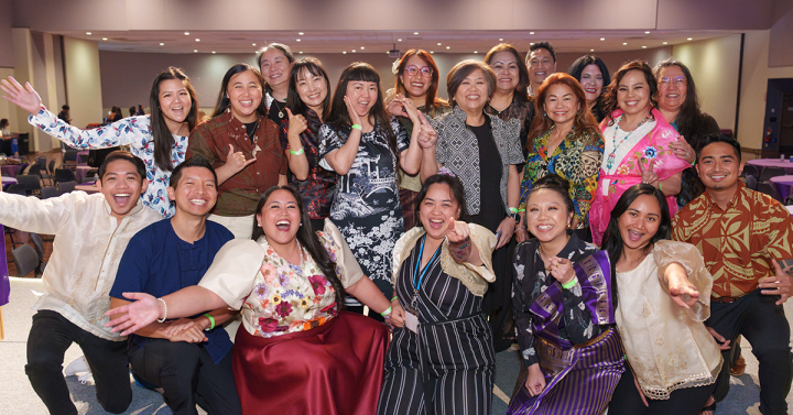20 people stand in two rows smiling at the camera is traditional Asian attire. 