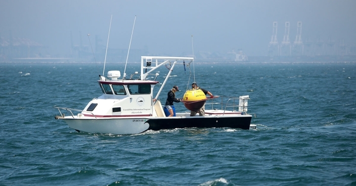 A yellow CDIP buoy is deployed from a small boat off the coast of California.