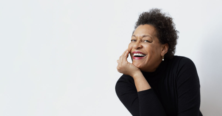 A seated woman dressed in black smiles at the camera against against a white background.