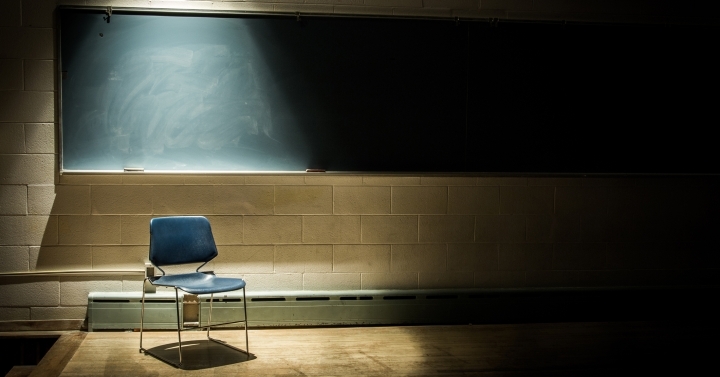 A solitary chair sits illuminated in lonely classroom in front of old-style chalkboard