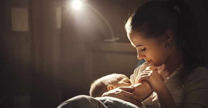 Woman breastfeeds baby with ray of light in the background.