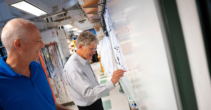 David Golomb and David Kleinfeld work out a problem on a whiteboard.