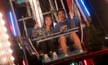 两名加州大学圣地亚哥分校的学生被拍到在节日期间乘坐摩天轮，周围灯光闪烁。