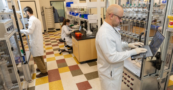 researchers in lab coats work at different stations in a laboratory