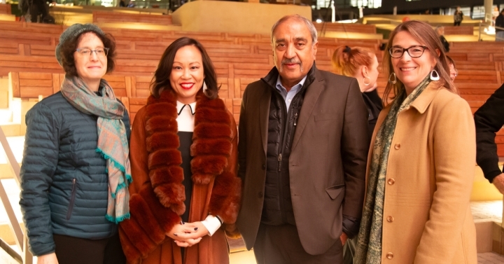 The four leaders are shown in formal winter wear, posing in front of the warmly lit seating of the Epstein Family Amphitheater. 