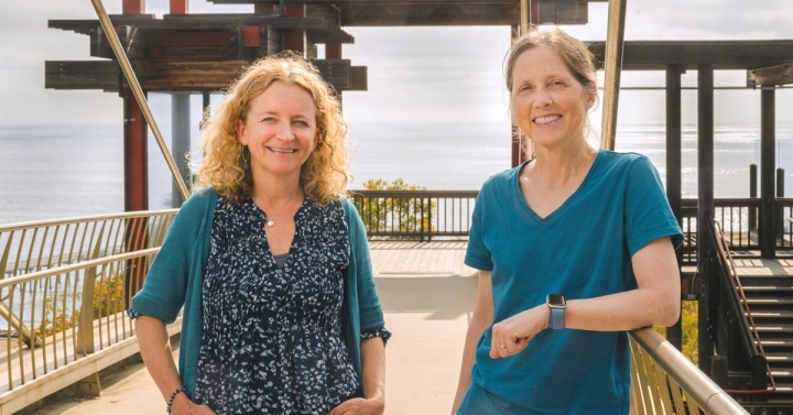 Two people standing outside with the ocean visible in the distance.