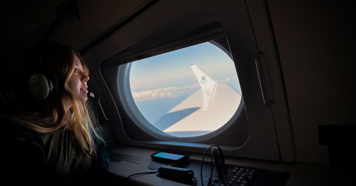 A woman looks out an airplane window where the wing of the aircraft is visible. Photo by Erik Jepsen, UC San Diego
