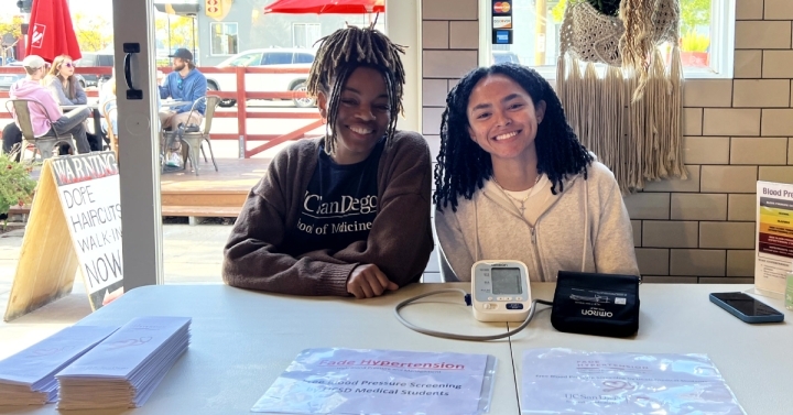 Two Black women sitting at a table smiling towards the camera. 