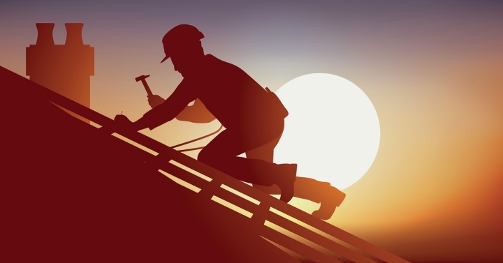 Silhouette of construction worker kneeling on roof with hammer with a large, blazing sun in the sky behind.