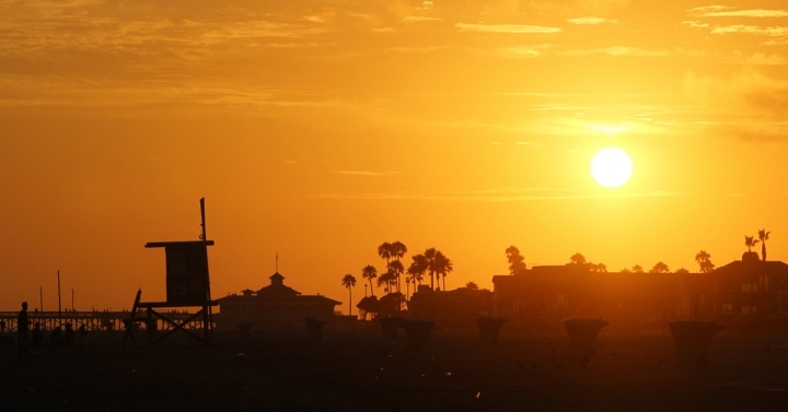 Lifeguard station and palm trees silhouetted against a rising sun in a yellow and orange sky