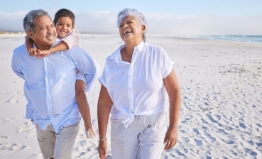 Two adult seniors walking on the beach with a child