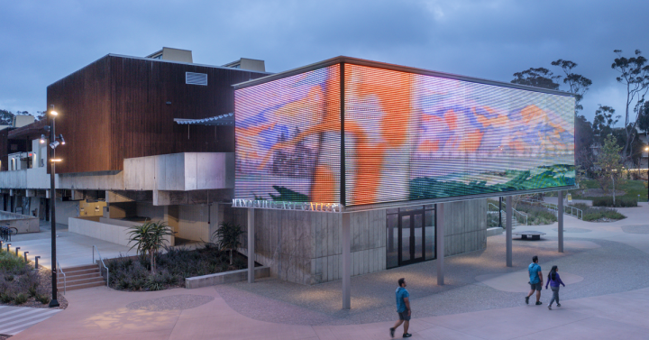 Exterior of the Mandeville Art Gallery in the evening with a video on the media mesh screen.