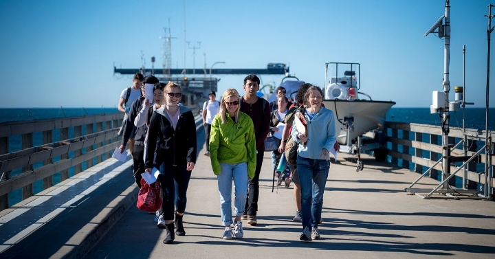 A professor and a group of 10 undergraduate students walk along a research pier.