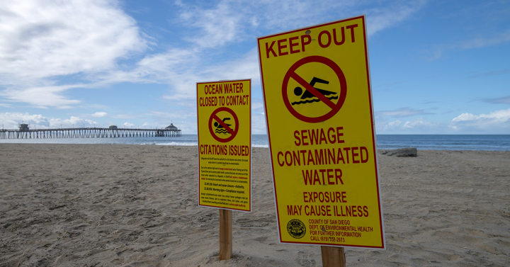 two yellow signs advising swimmers to keep out of ocean posted in the sand