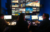 Video: Three people sit at a bank of monitors in a dark room