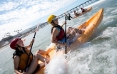 Two UC San Diego women students sitting in a tandem kayak paddling into the waves on La Jolla Shores beach.