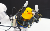 Robot hand holds a toy rubber duck in its palm.